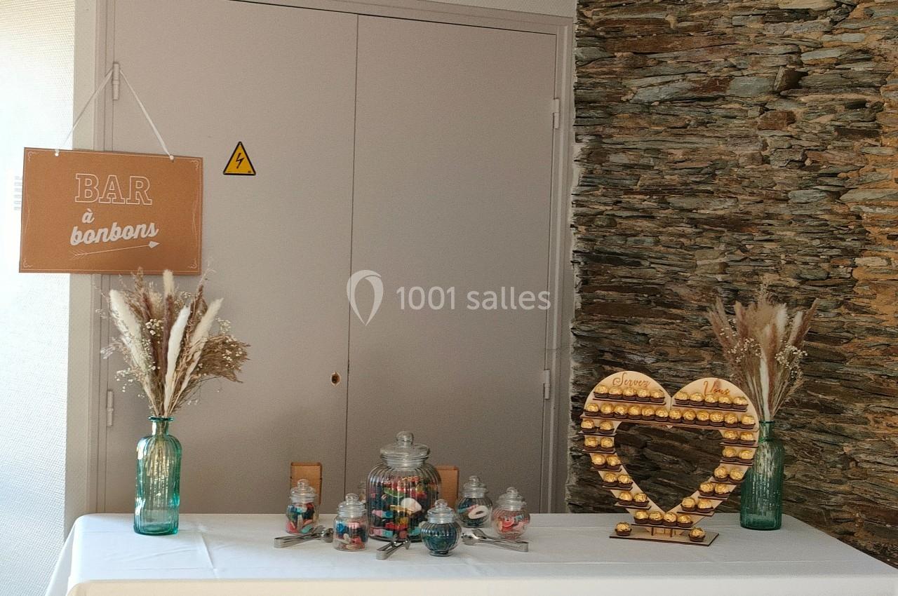 Table décorée avec un bar à bonbons, des pots en verre remplis de friandises et un cœur en bois sur un mur en pierre.