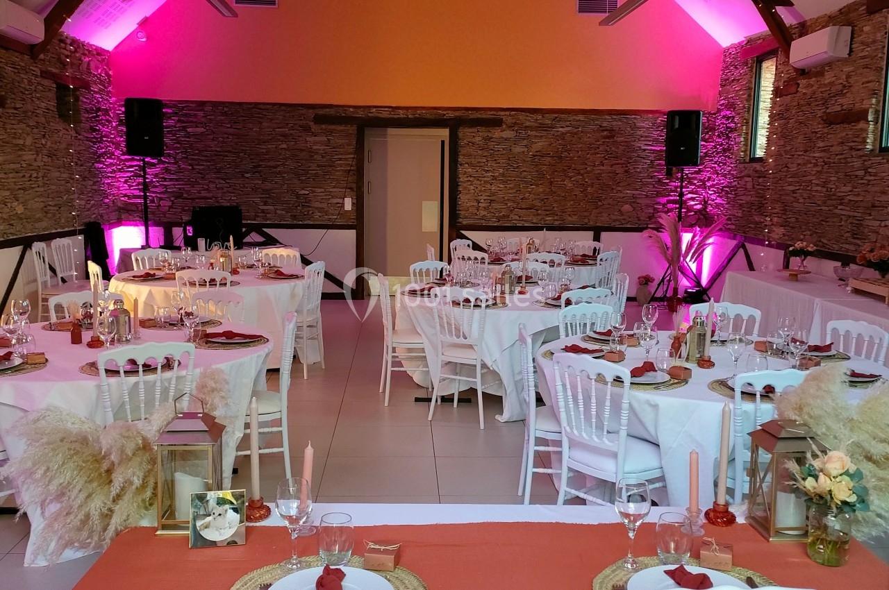 Salle de réception décorée avec des tables dressées, des guirlandes lumineuses suspendues et un éclairage rose.