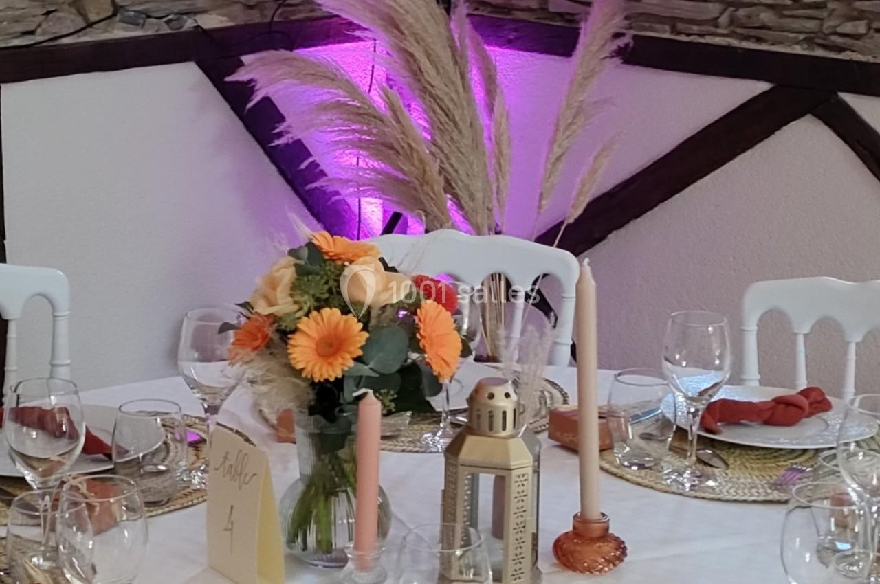 Table décorée pour un événement avec fleurs, bougies, lanternes et serviettes rouges, devant un mur en pierre éclairé.