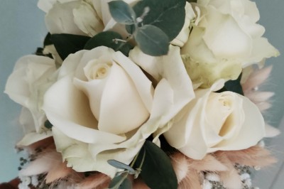 Voiture ancienne blanche décorée de fleurs, stationnée devant un bâtiment en pierre avec un toit en ardoise.