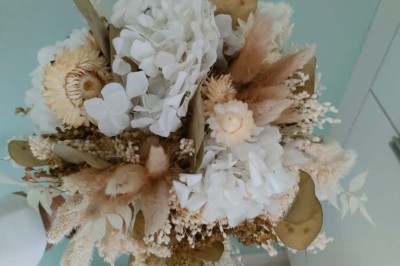 Voiture ancienne blanche décorée de fleurs, stationnée devant un bâtiment en pierre avec un toit en ardoise.