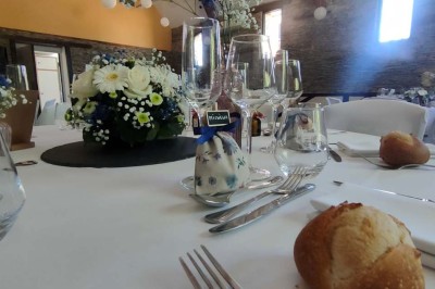 Voiture ancienne blanche décorée de fleurs, stationnée devant un bâtiment en pierre avec un toit en ardoise.