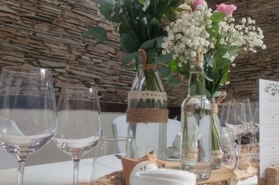 Voiture ancienne blanche décorée de fleurs, stationnée devant un bâtiment en pierre avec un toit en ardoise.