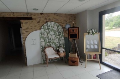 Voiture ancienne blanche décorée de fleurs, stationnée devant un bâtiment en pierre avec un toit en ardoise.