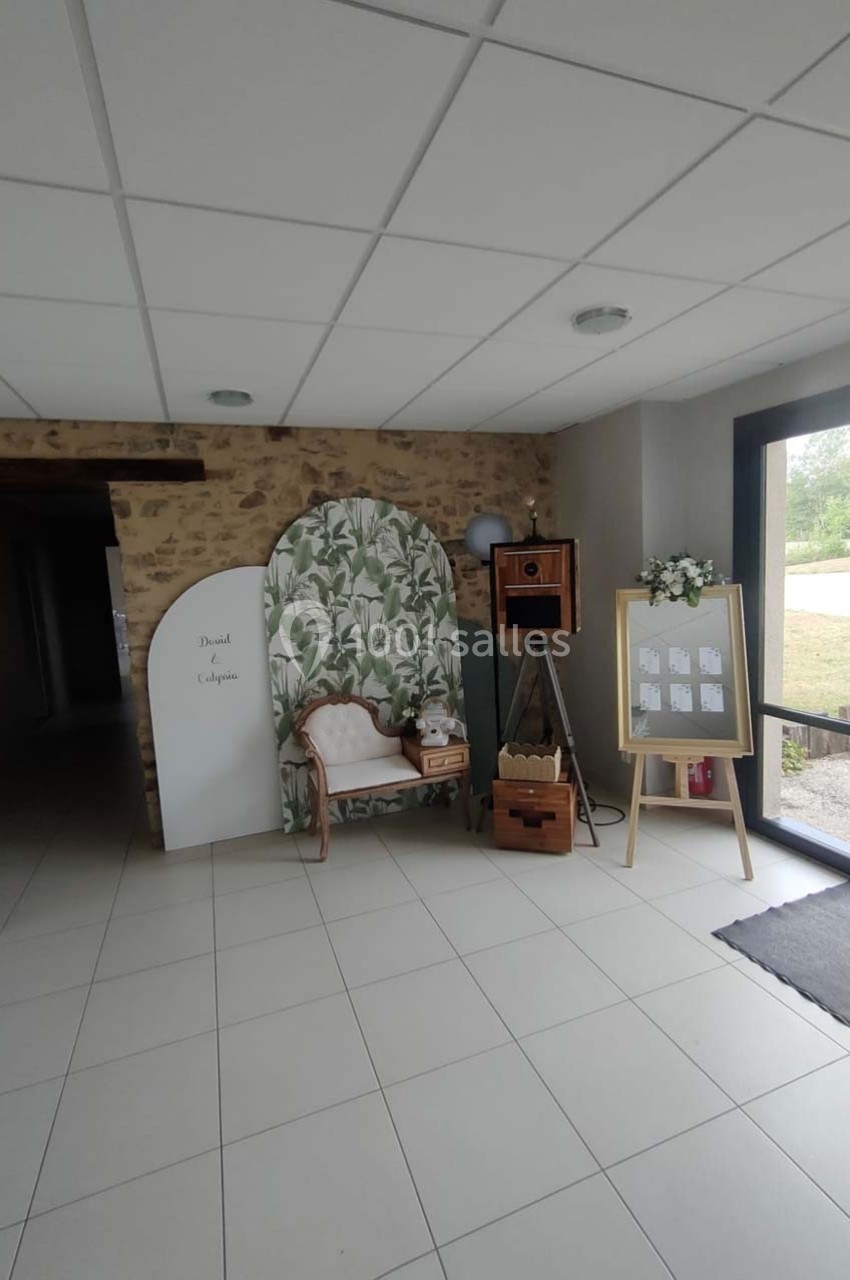 Coin décoratif avec fauteuil, paravent végétal, appareil photo vintage et tableau d'affichage près d'une baie vitrée.