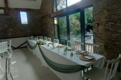 Voiture ancienne blanche décorée de fleurs, stationnée devant un bâtiment en pierre avec un toit en ardoise.