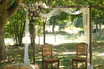 Voiture ancienne blanche décorée de fleurs, stationnée devant un bâtiment en pierre avec un toit en ardoise.