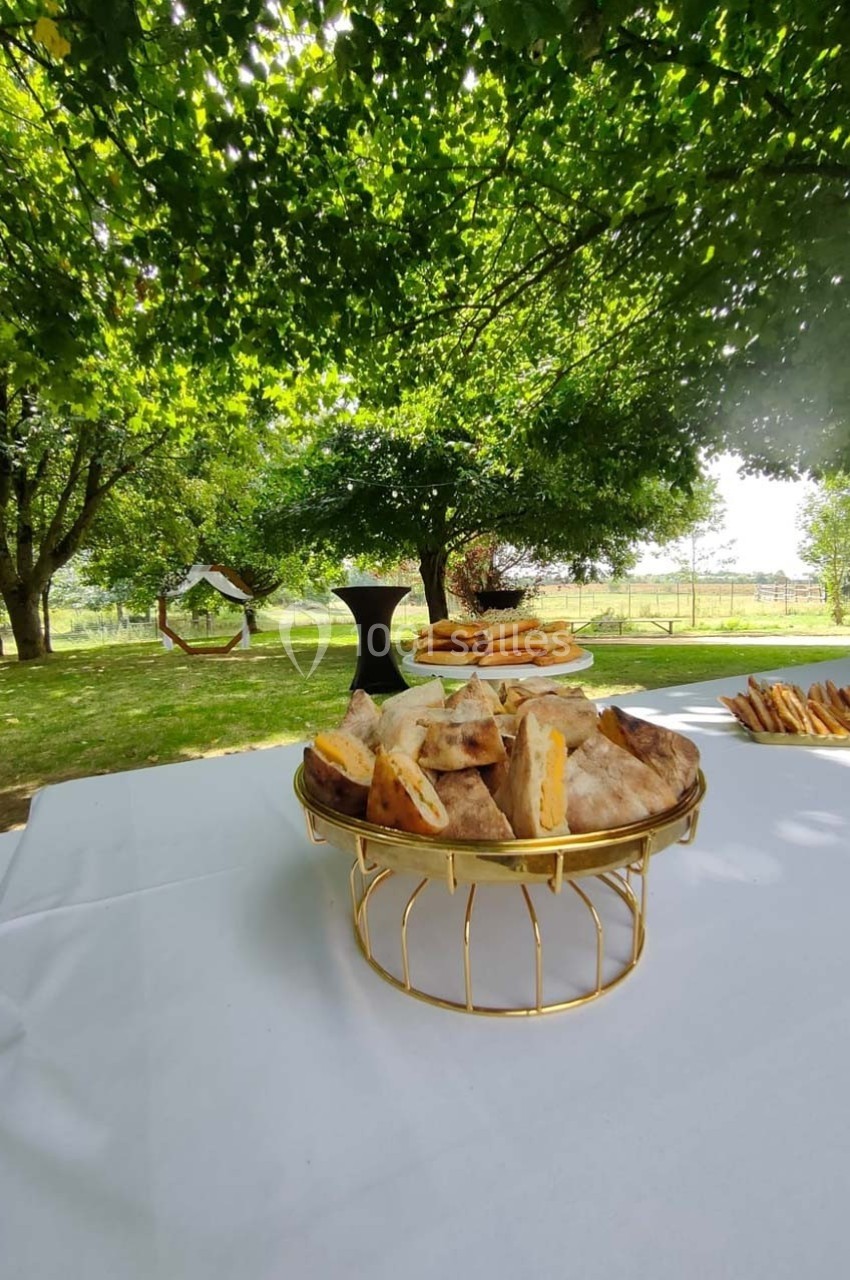 Plateau de sandwichs disposé sur une table blanche en extérieur, sous des arbres dans un cadre verdoyant.
