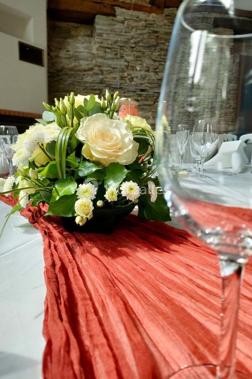 Centre de table floral avec roses blanches et feuillage, posé sur une nappe blanche et un chemin de table rouge plissé.