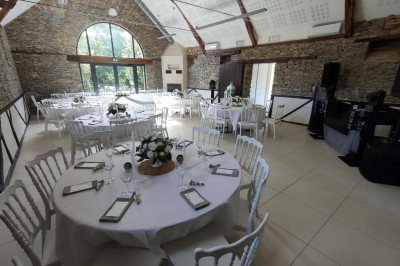 Voiture ancienne blanche décorée de fleurs, stationnée devant un bâtiment en pierre avec un toit en ardoise.