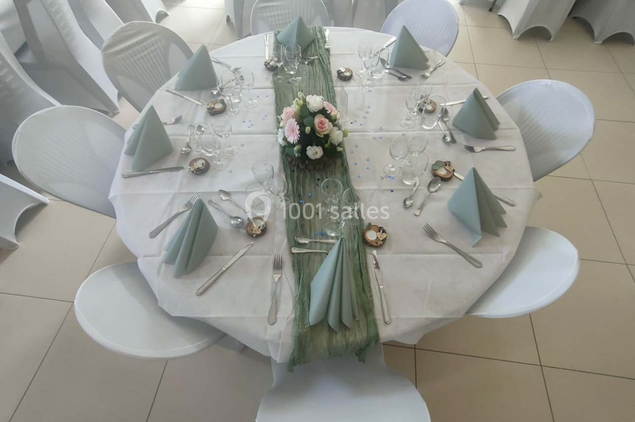 Table ronde dressée pour un événement, avec nappes blanches, serviettes pliées, centre floral et couverts disposés.