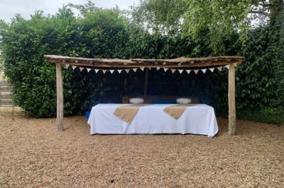 Voiture ancienne blanche décorée de fleurs, stationnée devant un bâtiment en pierre avec un toit en ardoise.