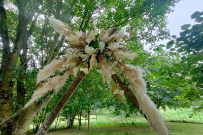 Voiture ancienne blanche décorée de fleurs, stationnée devant un bâtiment en pierre avec un toit en ardoise.