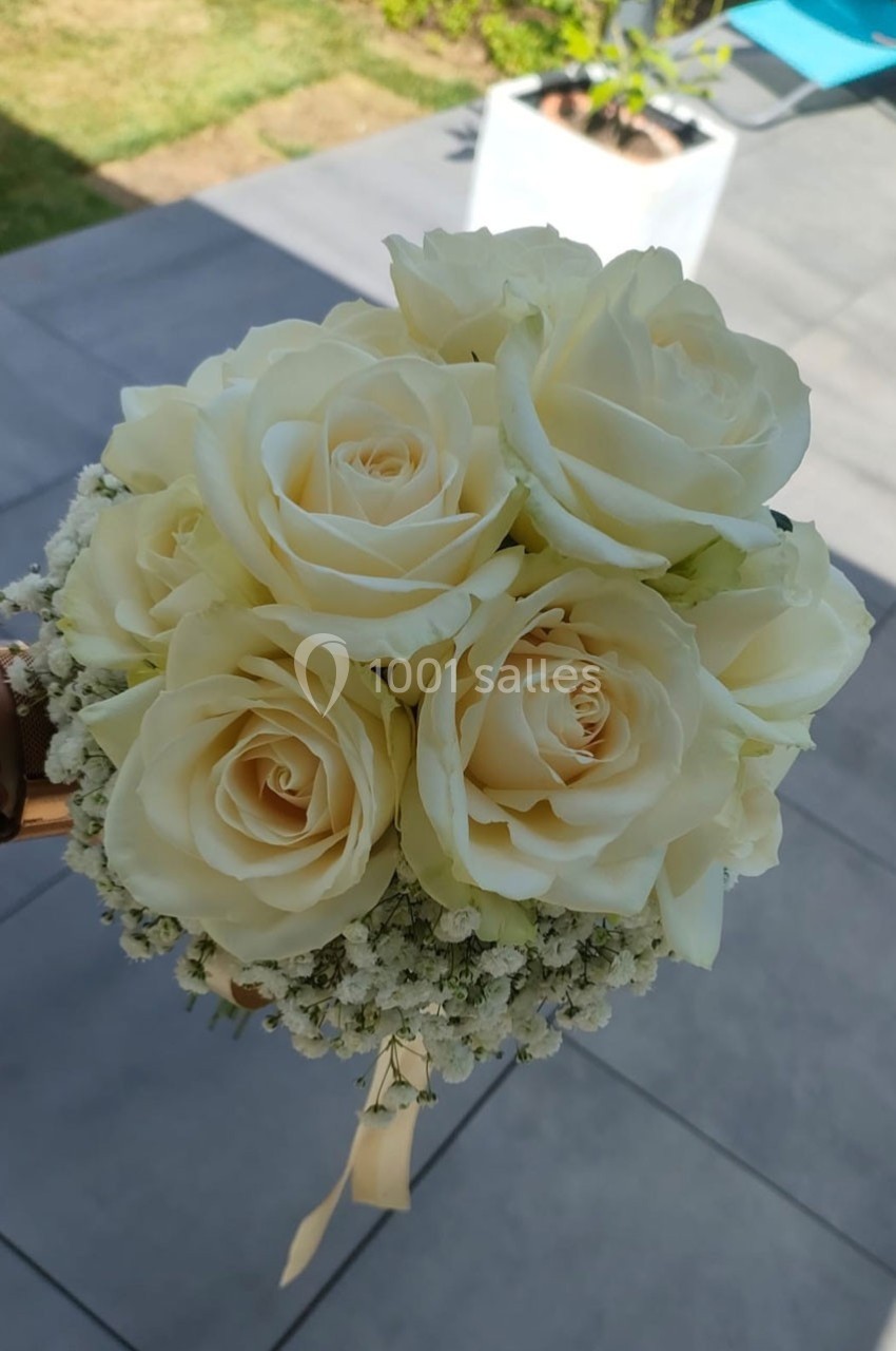 Bouquet de roses blanches entouré de gypsophile, tenu à la main sur une terrasse ensoleillée.