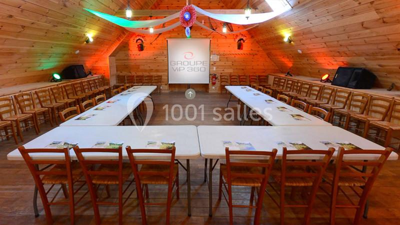 Salle de réunion en bois avec tables disposées en U, chaises alignées et écran de projection au fond.