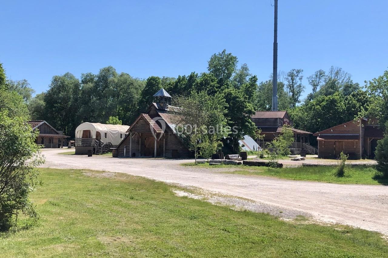 Village en plein air avec bâtiments en bois, une yourte, un chemin de terre et des arbres sous un ciel dégagé.