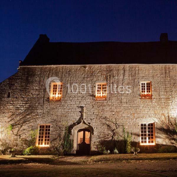 Façade en pierre d'une maison ancienne éclairée par des lumières chaudes, photographiée de nuit.