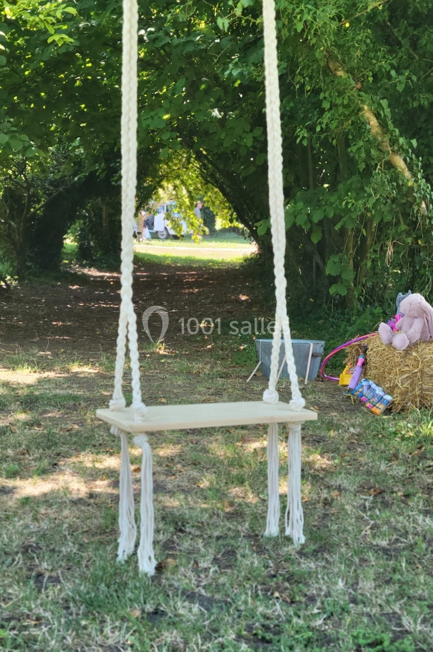 Une balançoire en corde suspendue sous des arbres, avec des jouets et un chemin en arrière-plan.