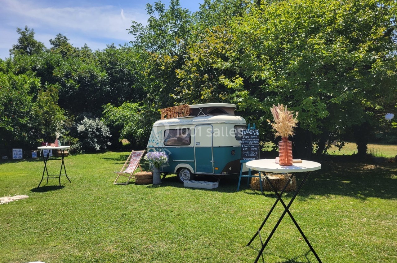 Caravane vintage installée sur une pelouse verdoyante, entourée de tables décorées et d'arbres en arrière-plan.