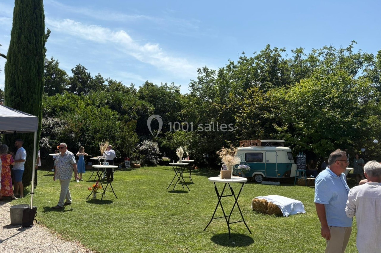 Personnes discutant dans un jardin avec des tables hautes décorées, un food truck vintage et des arbres en arrière-plan.