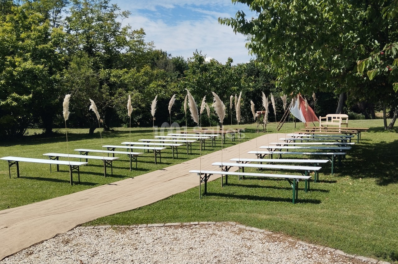 Allée centrale bordée de bancs et tables en bois, installée sur une pelouse avec des arbres et des décorations végétales.