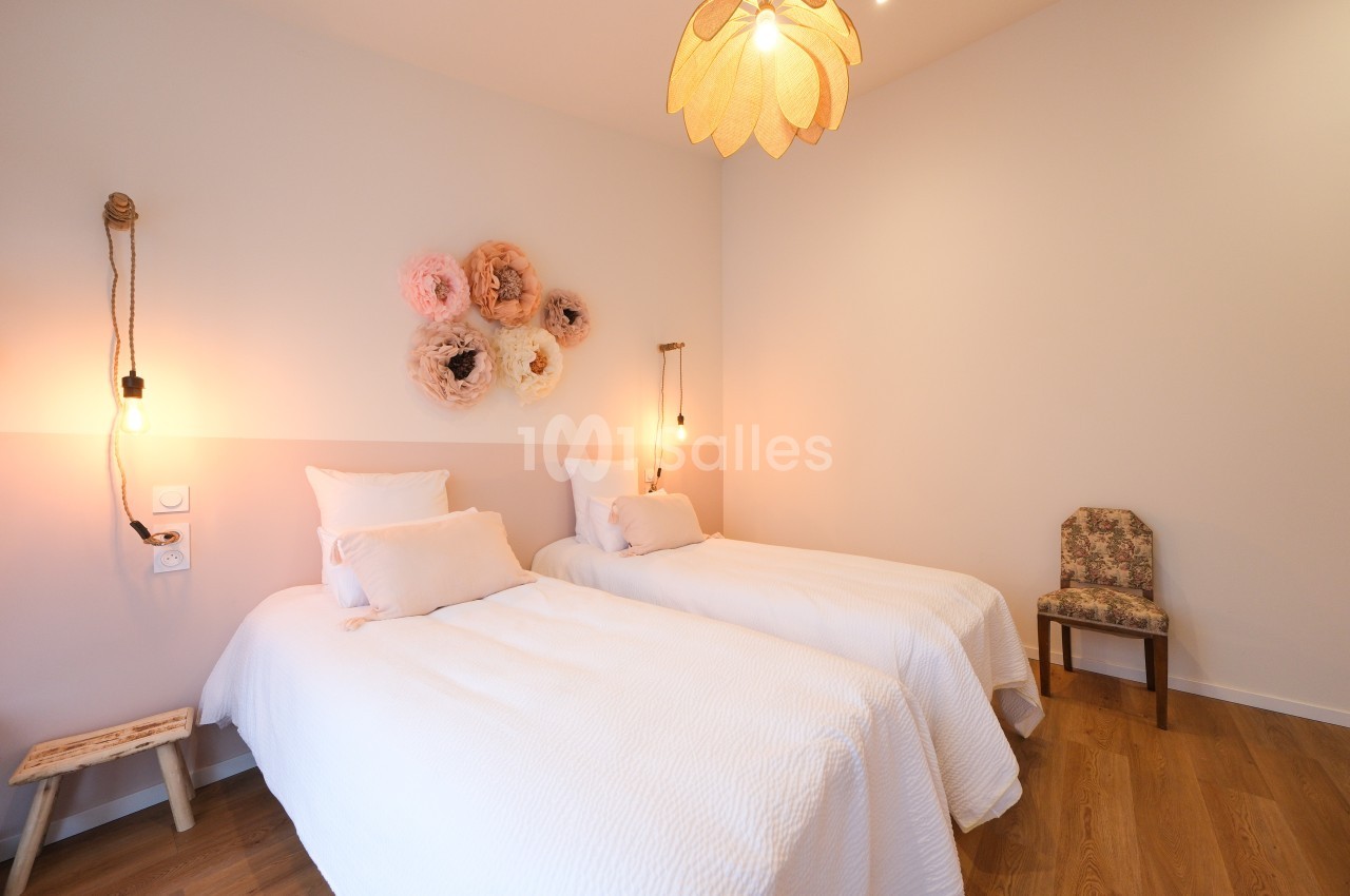 Deux lits simples avec linge blanc dans une chambre lumineuse, décorée de fleurs murales et éclairée par des suspensions.