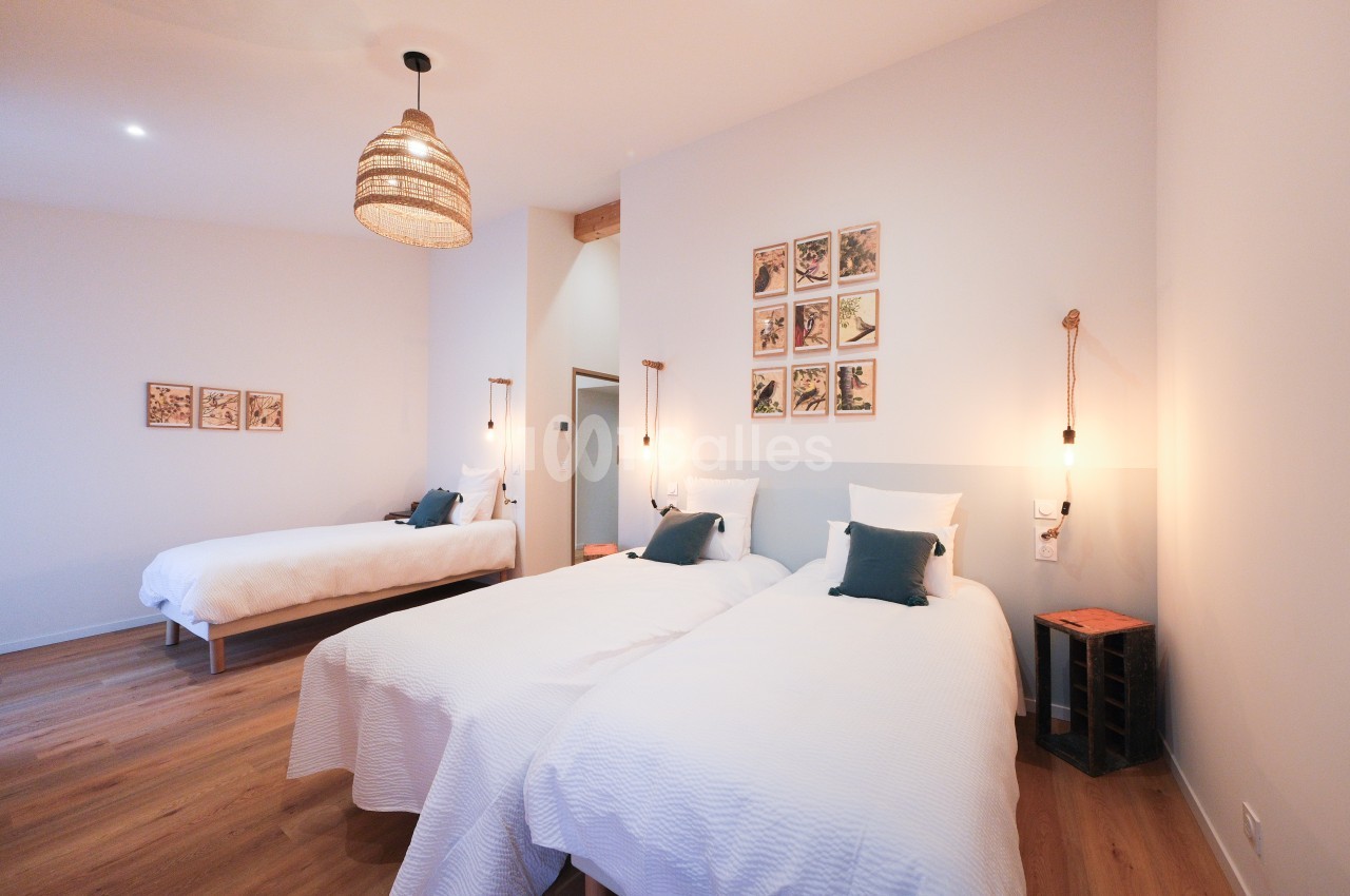 Chambre lumineuse avec trois lits, parquet en bois, décor minimaliste et suspensions en corde.