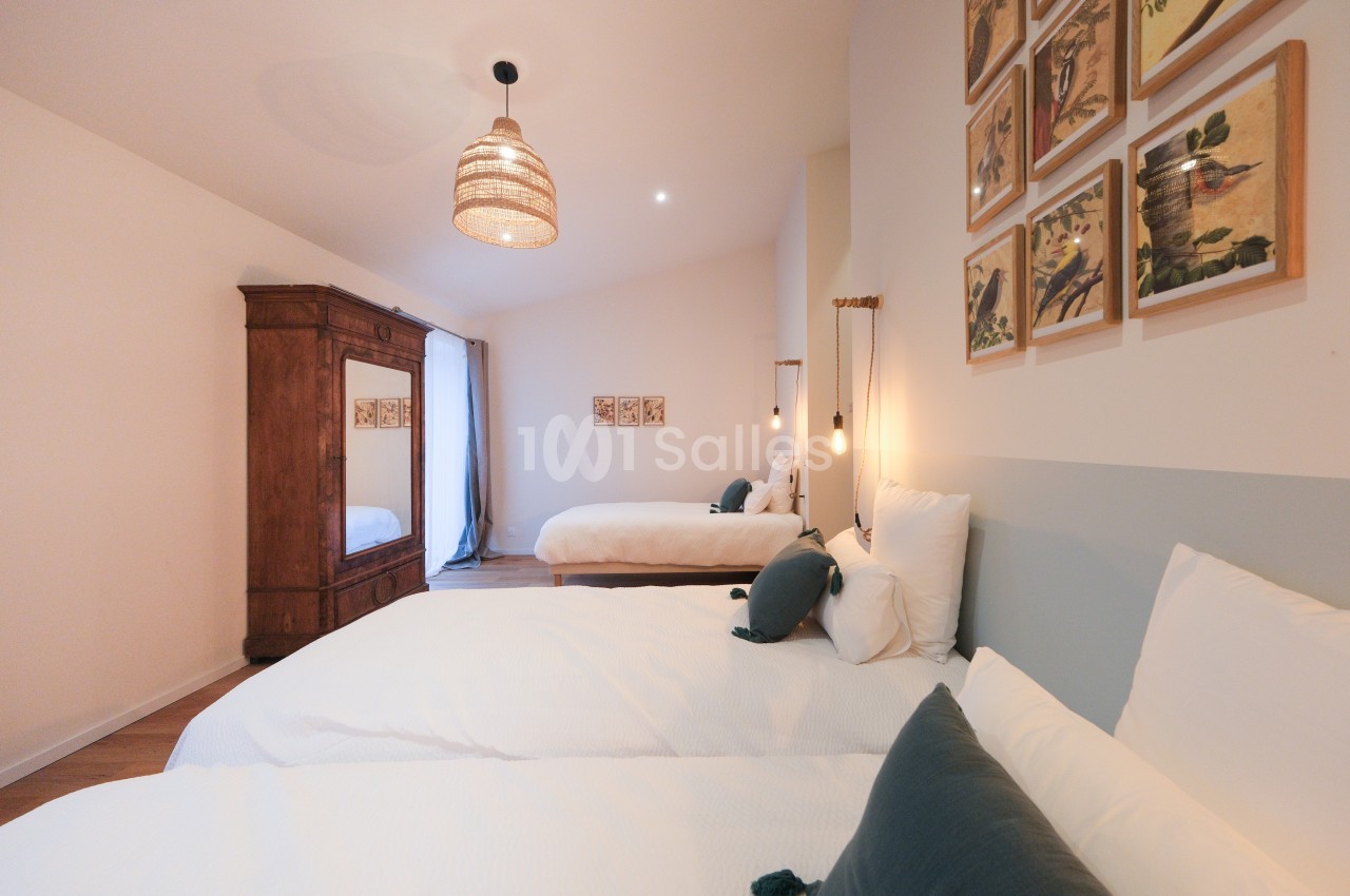 Chambre lumineuse avec deux lits, armoire en bois, suspension en osier et décorations murales.