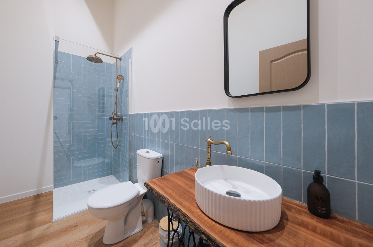 Salle de bain moderne avec douche à l'italienne, lavabo rond sur un meuble en bois et carrelage bleu.