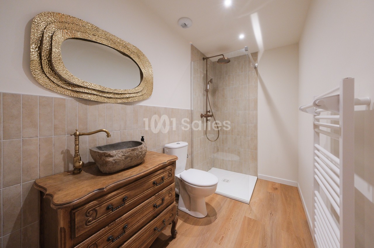 Salle de bain avec meuble en bois, vasque en pierre, miroir doré, douche à l'italienne et sèche-serviettes.