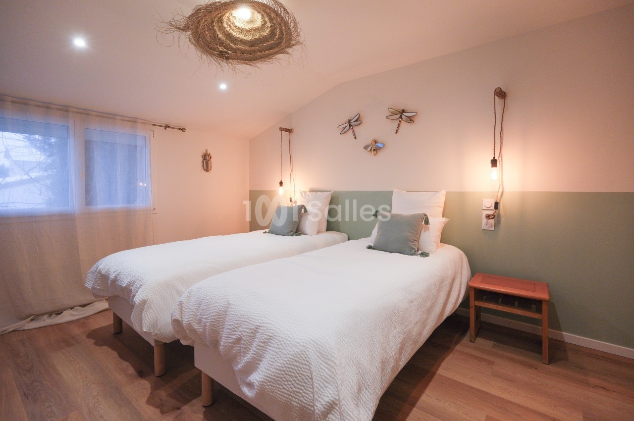 Deux lits simples avec linge blanc dans une chambre lumineuse, décorée de tons pastel et d'éléments naturels.