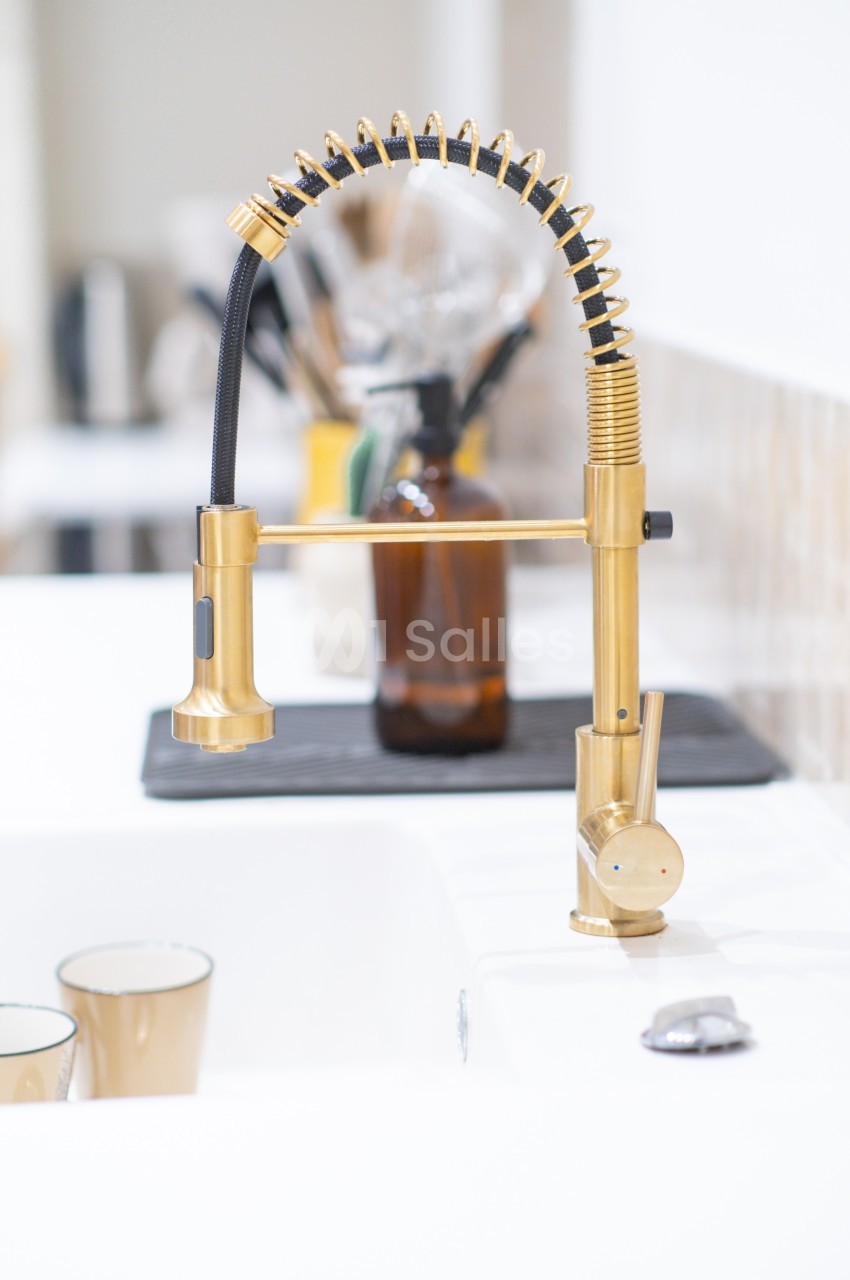 Robinet de cuisine doré au design moderne avec douchette flexible, installé sur un évier blanc.
