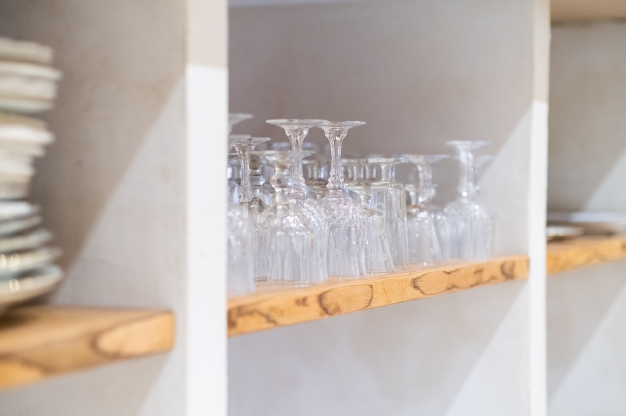 Verres à pied transparents alignés sur une étagère en bois dans un espace de rangement lumineux.
