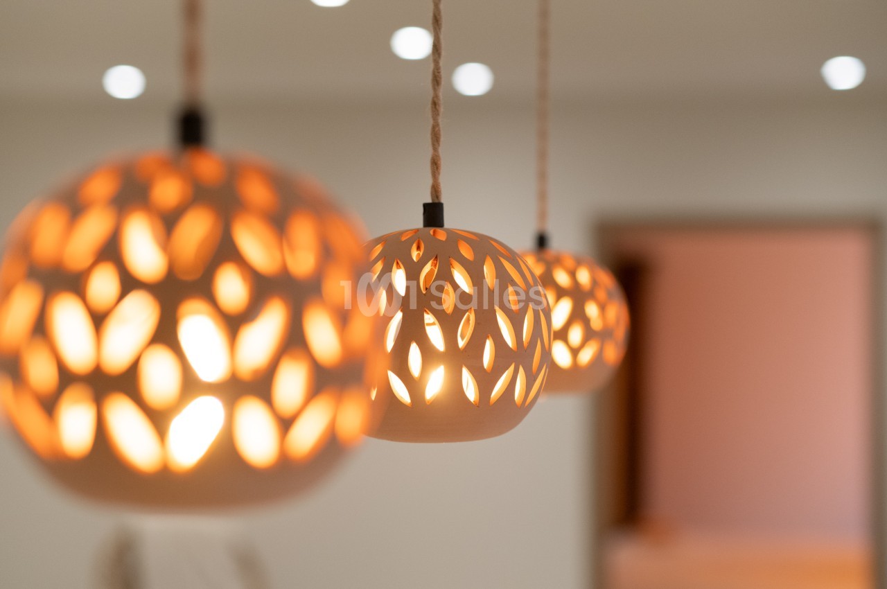 Suspensions lumineuses en céramique ajourée diffusant une lumière chaude dans un intérieur minimaliste.