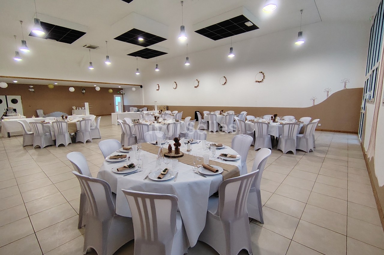 Salle de réception décorée avec des tables rondes dressées, nappes blanches et chaises assorties.