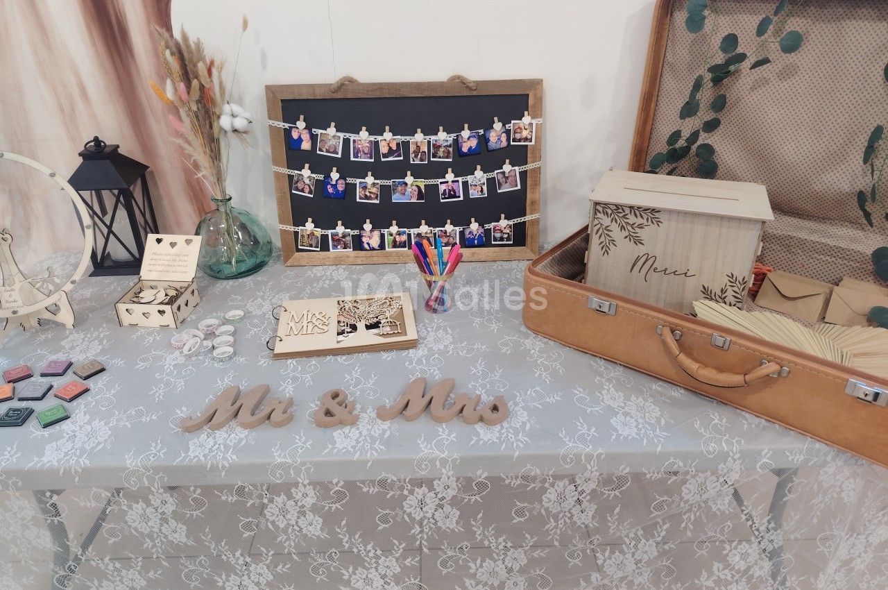 Table décorée pour un mariage avec valise vintage, livre d'or, photos suspendues et accessoires de papeterie.