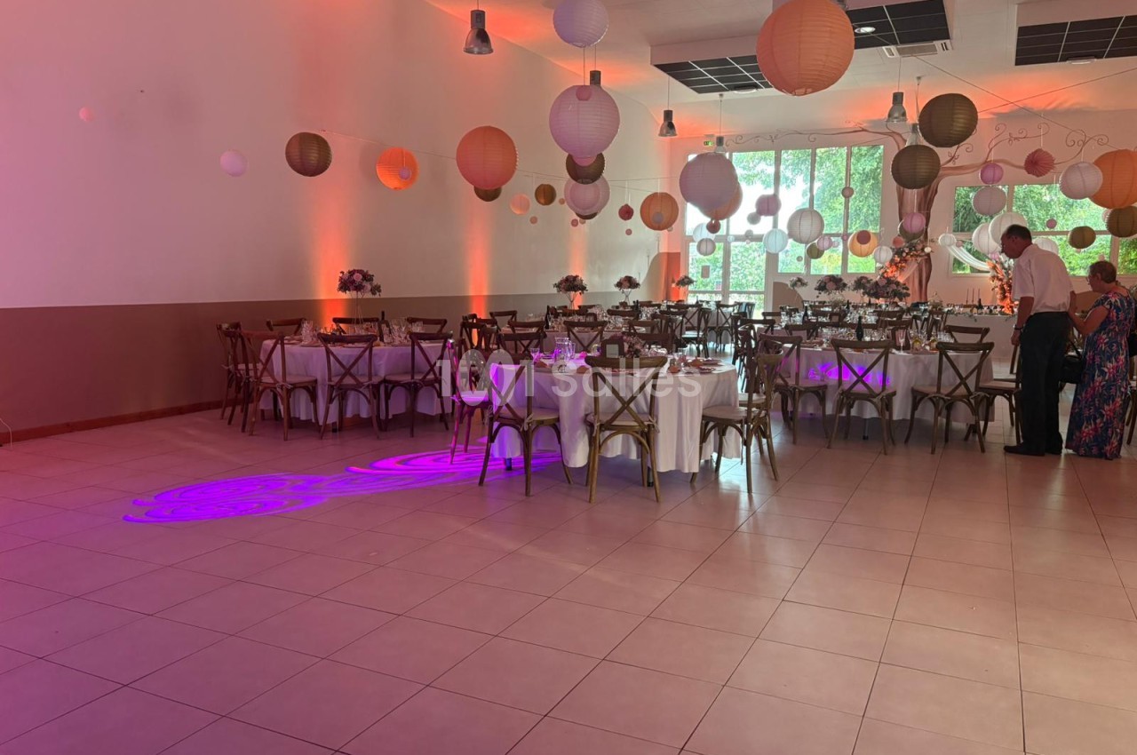 Salle de réception décorée avec des lanternes suspendues, des tables dressées et un éclairage tamisé.