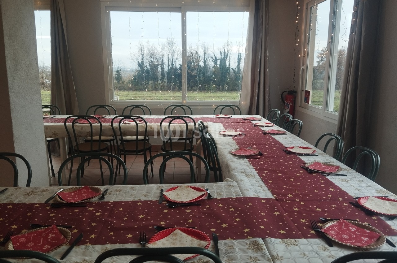 Salle décorée avec des tables alignées, nappes rouges et blanches, et assiettes disposées pour un repas festif.