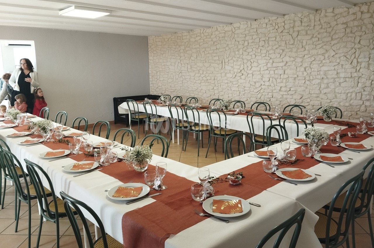 Salle décorée pour un repas avec des tables en U, nappes blanches et chemins de table orange, chaises vertes.