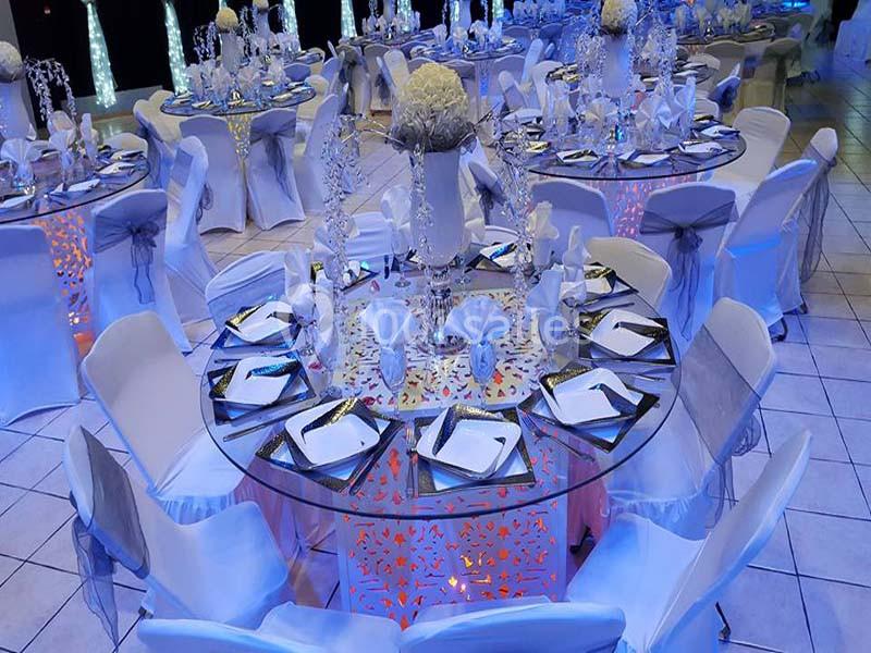 Salle de réception décorée avec des tables rondes ornées de nappes blanches, vaisselle élégante et centres de table floraux.