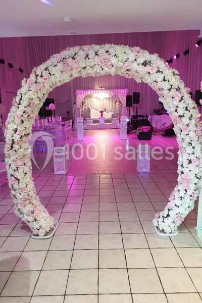 Arc de fleurs blanches et roses décorant une salle de réception avec éclairage rose et disposition festive.
