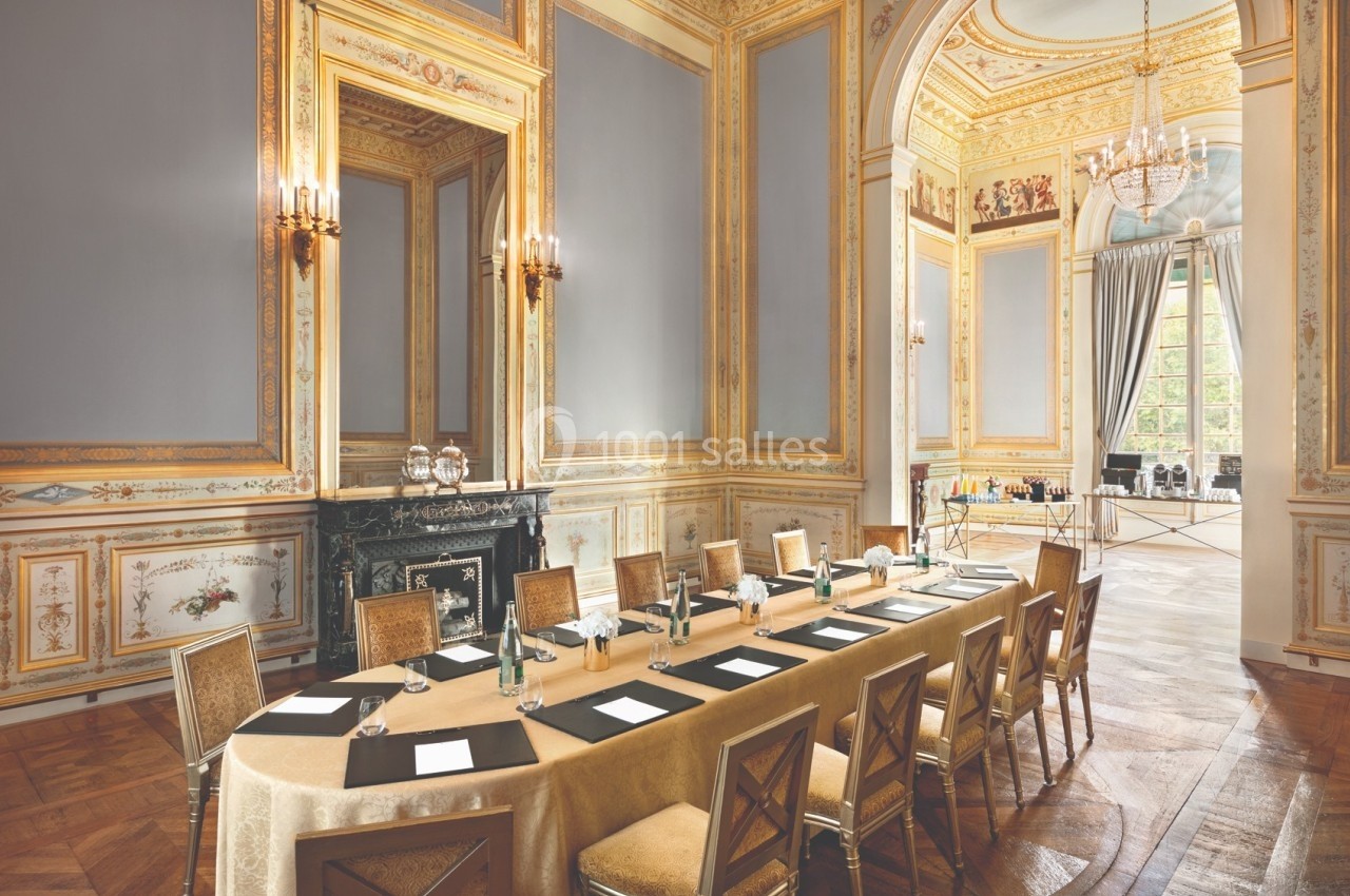 Salle de réunion élégante avec table rectangulaire, chaises en bois, murs ornés et grande fenêtre laissant entrer la lumière.