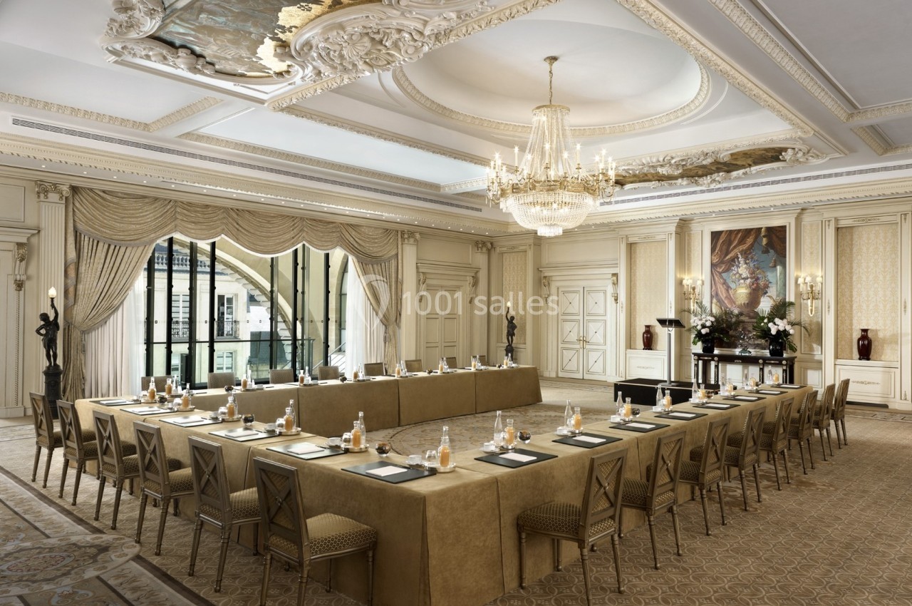 Salle de réunion élégante avec tables en U, chaises assorties, lustre imposant et décorations classiques.