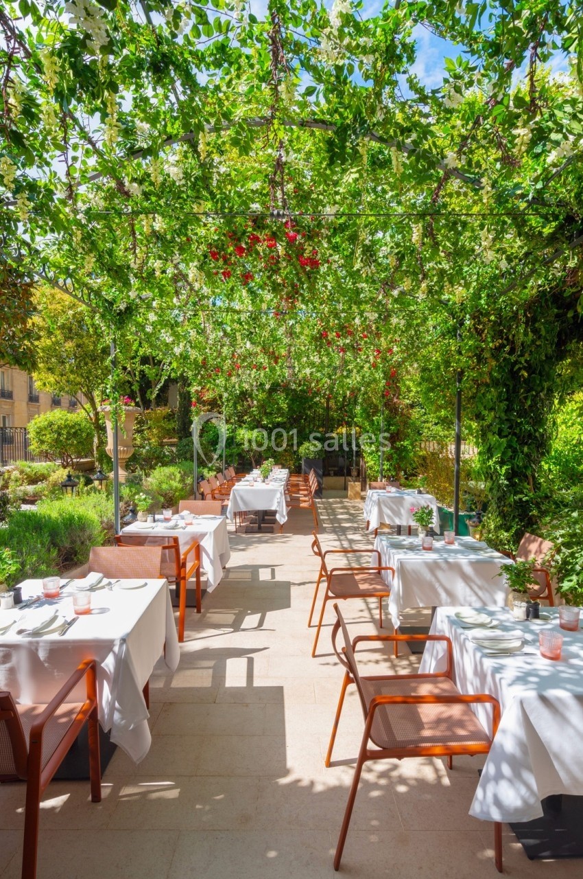 Terrasse de restaurant ombragée par une pergola végétalisée, avec des tables dressées et des chaises en bois.
