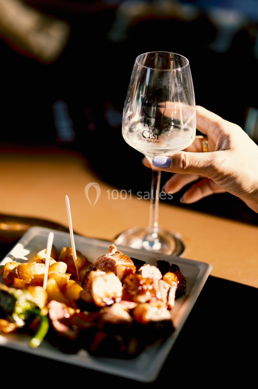 Une main tenant un verre de vin blanc près d'une assiette de viande grillée et de légumes sur une table.