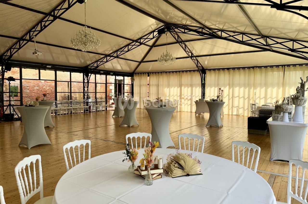Salle de réception lumineuse avec tables rondes et mange-debout, décorée de fleurs et éclairée par des lustres.