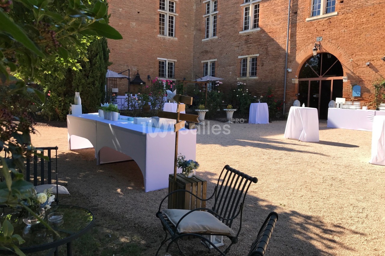 Cour extérieure d'un bâtiment en briques, aménagée pour un événement avec tables dressées et chaises disposées.