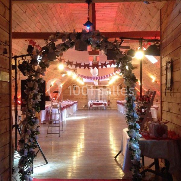 Salle de réception en bois décorée avec des guirlandes lumineuses, des fleurs et des tables dressées pour un événement.