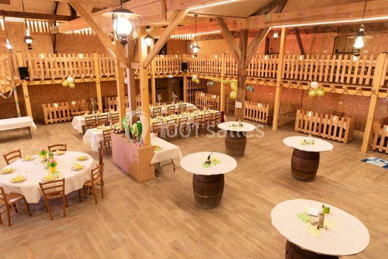 Salle de réception en bois avec tables rondes et rectangulaires décorées, éclairée par des suspensions.