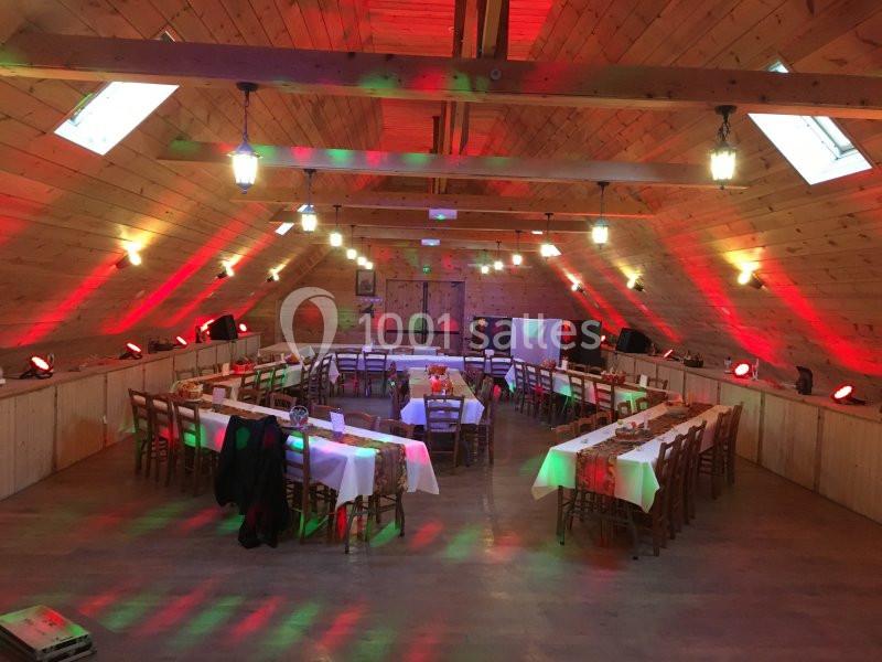 Salle en bois avec tables dressées en U, éclairage coloré et ambiance festive.